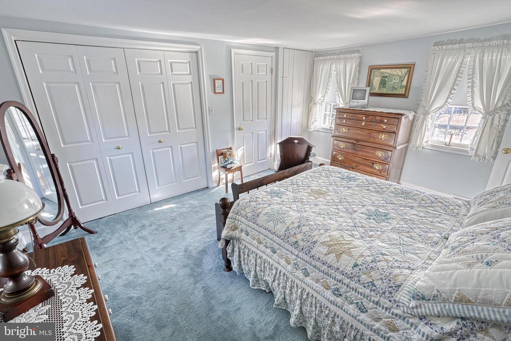 Bedroom with a patterned quilt, blue carpet, paneled closet doors, and wooden dresser.