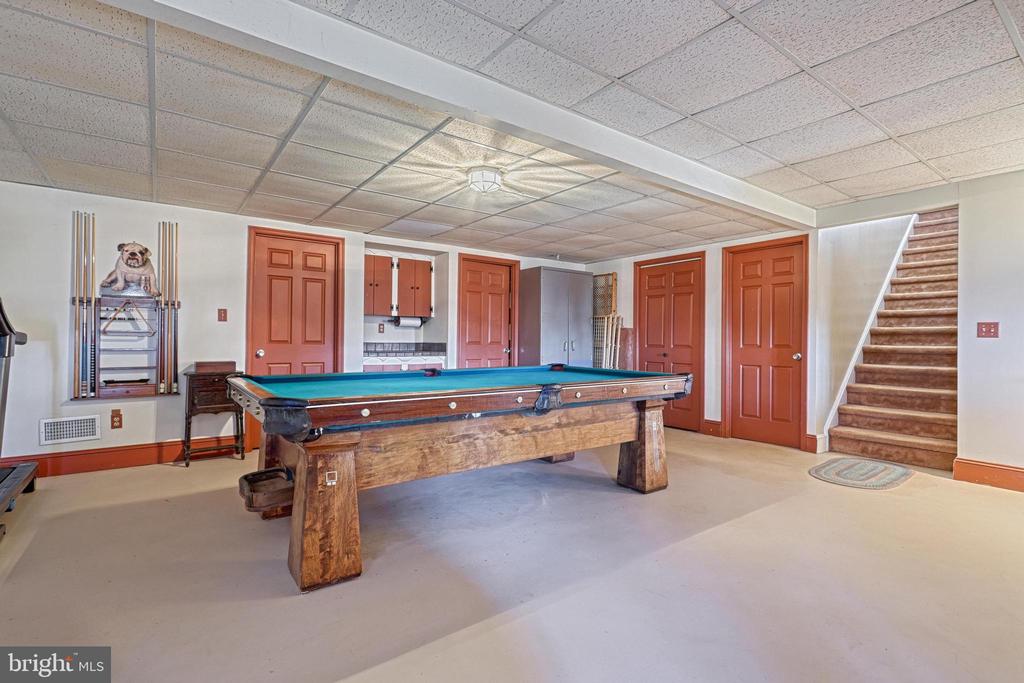 Basement game room with a wooden pool table, cue rack, and carpeted stairs.