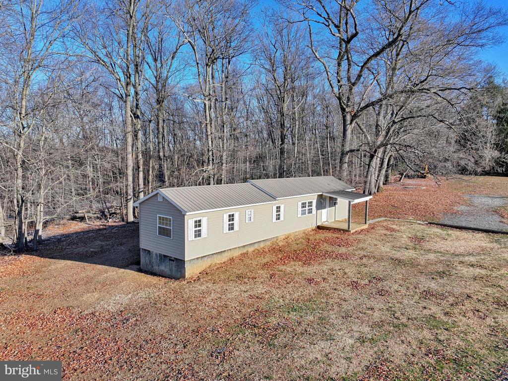 Single-story manufactured home with a covered entry sits in a leaf-strewn clearing among bare trees.