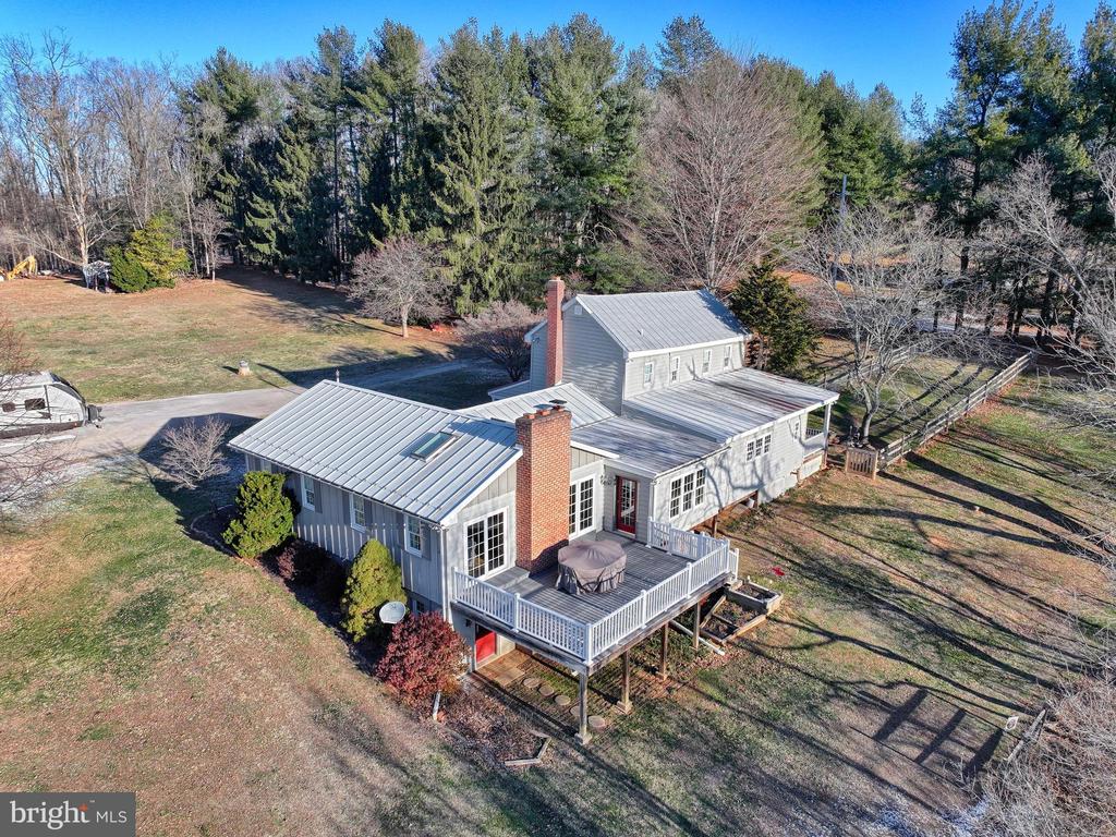 Aerial view of a gray two-story home with metal roofs and a raised deck on a wooded lot.