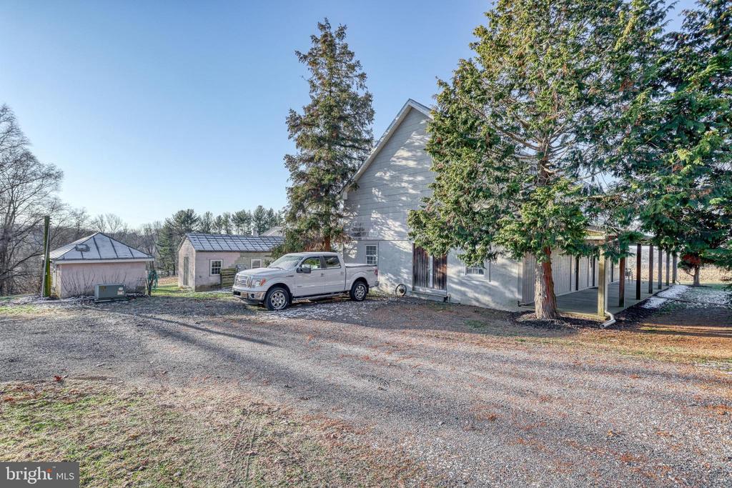 Gray house with a long covered porch, detached outbuilding, and pickup truck on the gravel driveway.