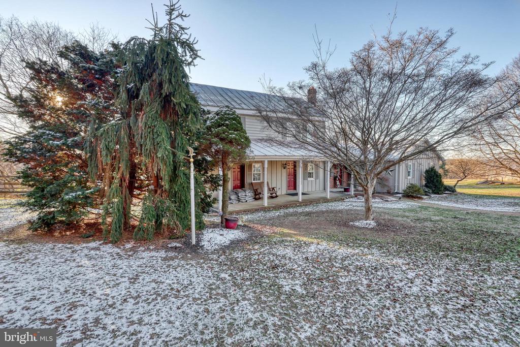 Long house with a covered porch and red doors in a lightly snow-covered yard.