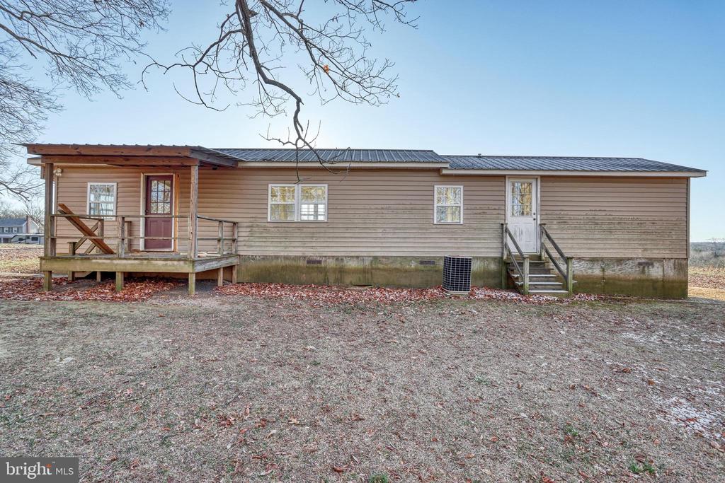 Single-story tan-sided home with a dark metal roof, front porch, and open winter yard.
