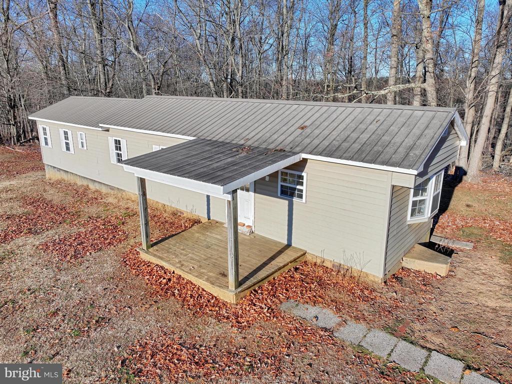 Beige single-story house with metal roofs, a covered deck, and a wooded yard.