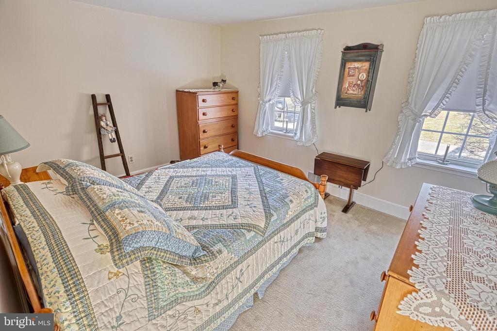 Bedroom with a patchwork quilt on a wooden bed, matching dressers, and lace curtains.