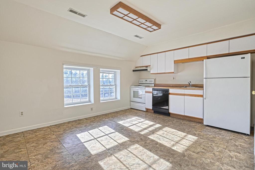Unfurnished kitchen with white appliances, wood-trimmed cabinets, two windows, and patterned tile flooring.