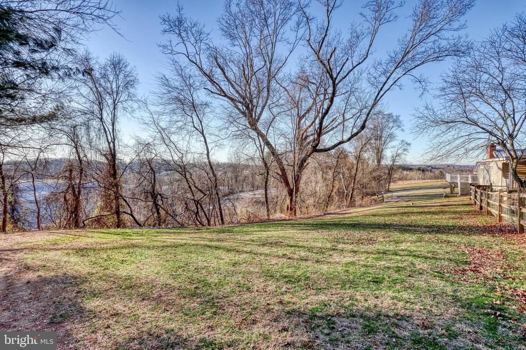 Grassy yard overlooking water, with leafless trees and a fenced deck beside the house.