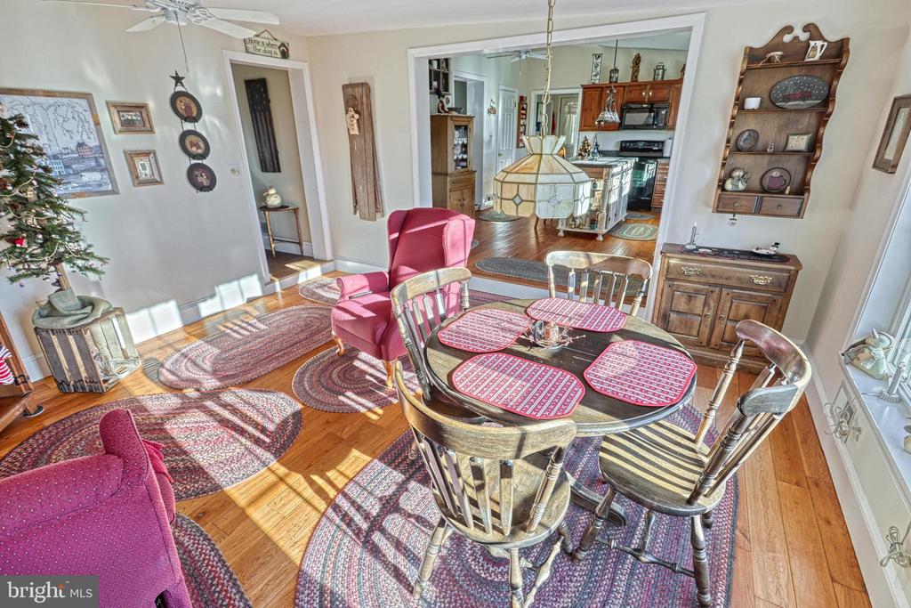 Dining room with a round wooden table, red placemats, patterned rugs, and an open view into the kitchen.
