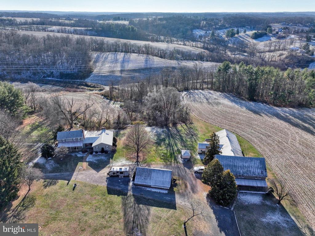Aerial view of a rural property with several buildings amid snowy fields and leafless woods.
