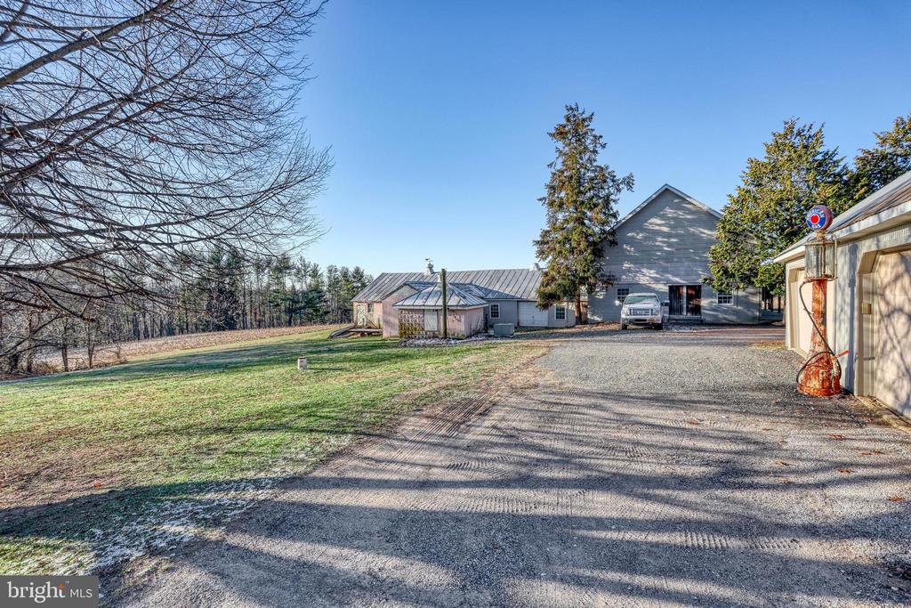 Gray house and outbuildings beside a broad gravel driveway and bare trees.