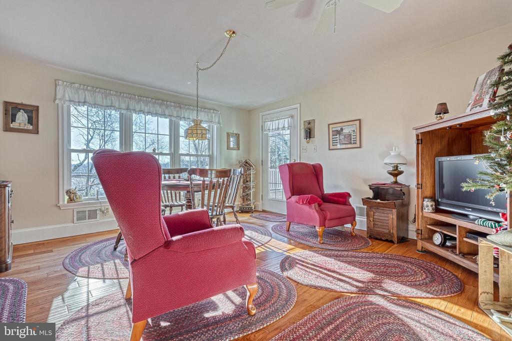 Furnished living room with red armchairs, hardwood floors, and a dining area by large windows.