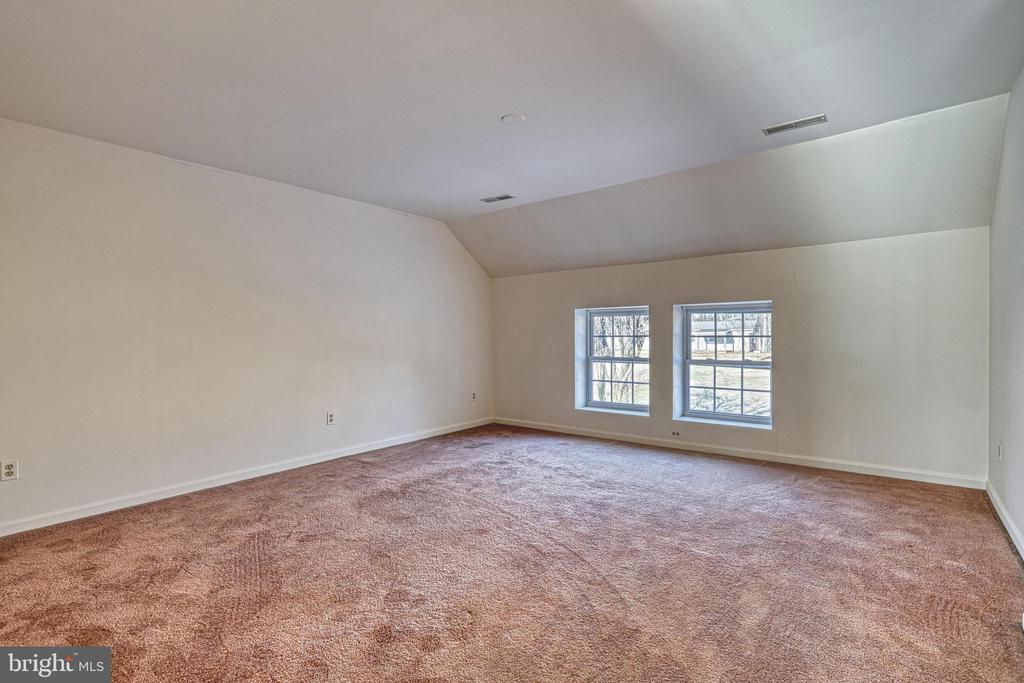 Empty carpeted room with a high sloped ceiling and two windows.