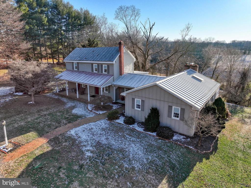 Aerial view of a gray two-story home with metal roofs, covered porch, and attached garage.