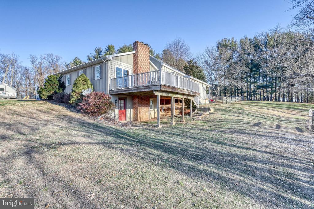 Gray-sided house with a raised deck and brick chimney overlooking a sloping lawn.