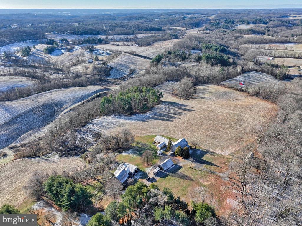 Aerial view of farm buildings surrounded by open fields and wooded countryside with patches of snow.