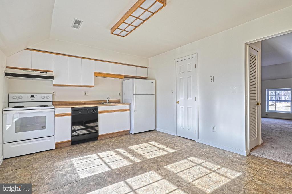 Unfurnished kitchen with white cabinets, contrasting appliances, and sunlight across the patterned floor.
