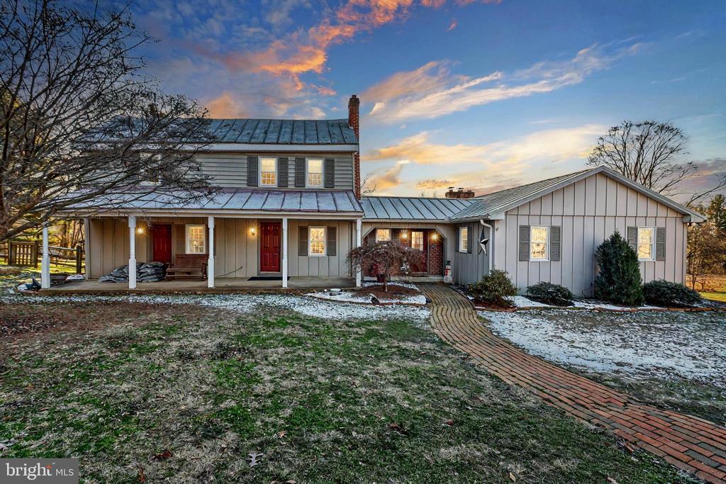 Gray-sided home with metal roofs and a curving brick walkway at sunset.