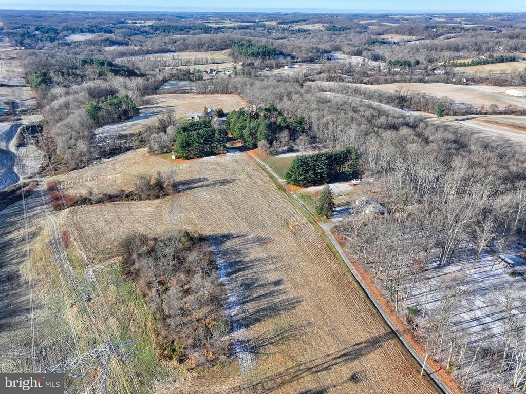 Aerial view of an open field bordered by woods and evergreen trees amid rural farmland.