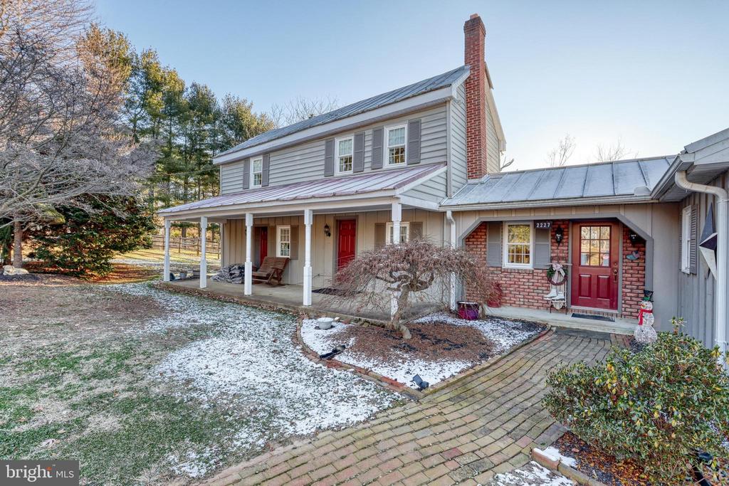 Gray two-story home with a metal roof, covered porch, red doors, and a lightly snow-covered yard.