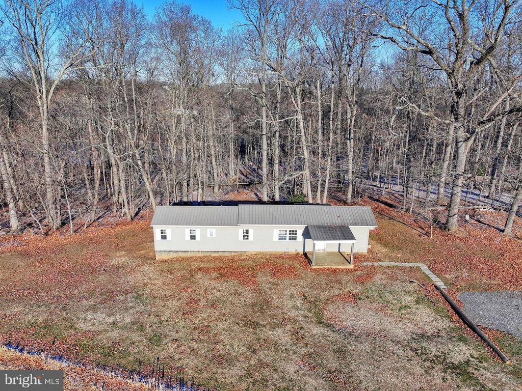 Aerial view of a single-story home in a wooded clearing, with a covered entry and gravel driveway.