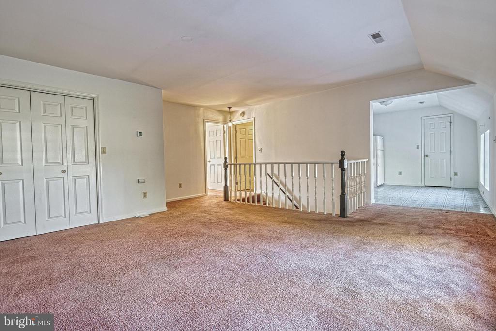 Carpeted room with double closets, a stairwell railing, and an adjoining tiled area.