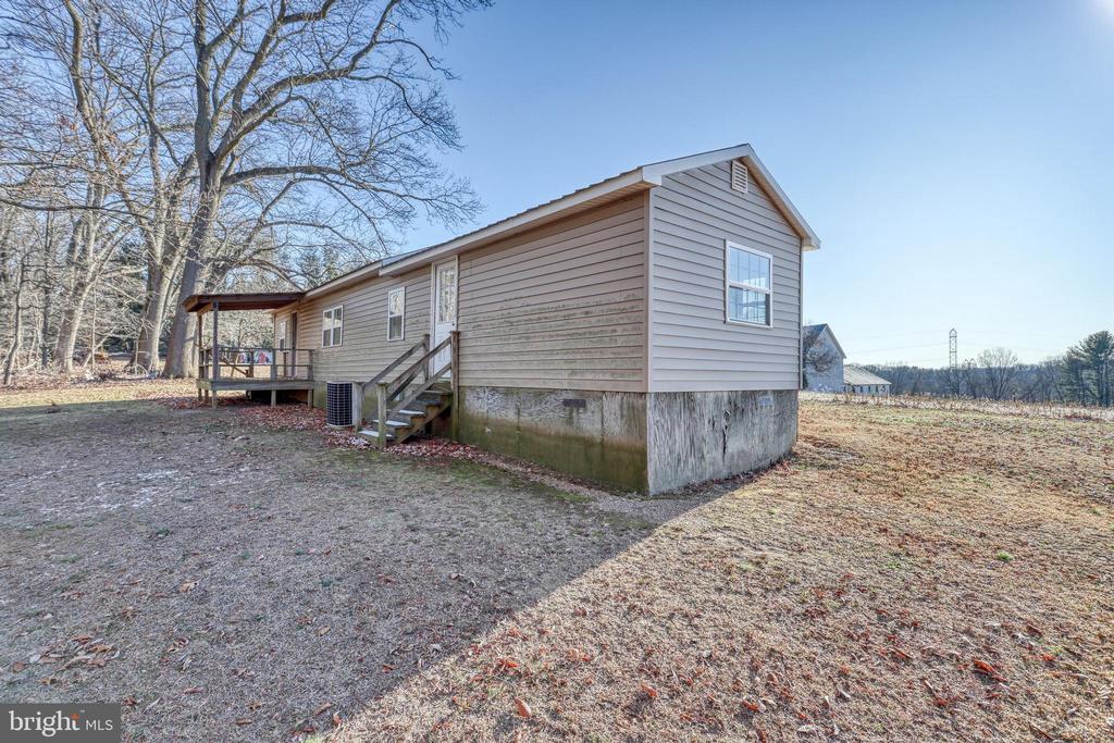 Beige-sided home with a raised foundation, porch, and steps beside a leafless yard.