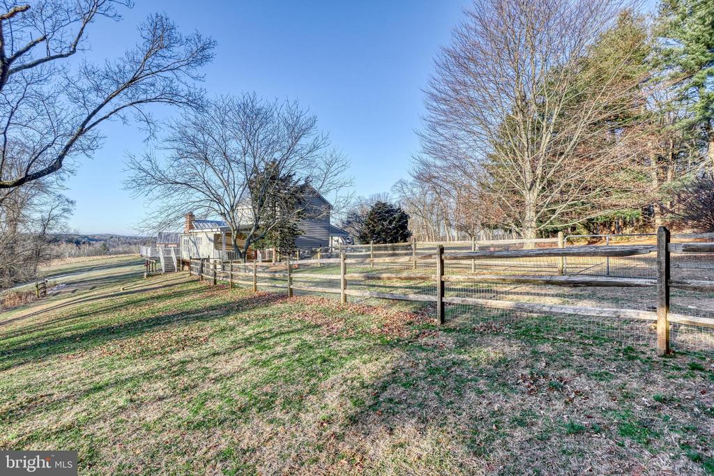 Gray house beyond a fenced, sloping yard, with leafless trees and countryside views.