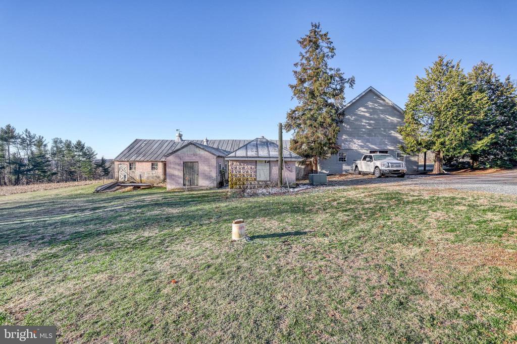 Rural property with a gray gabled building, smaller outbuildings, and a broad grassy yard.