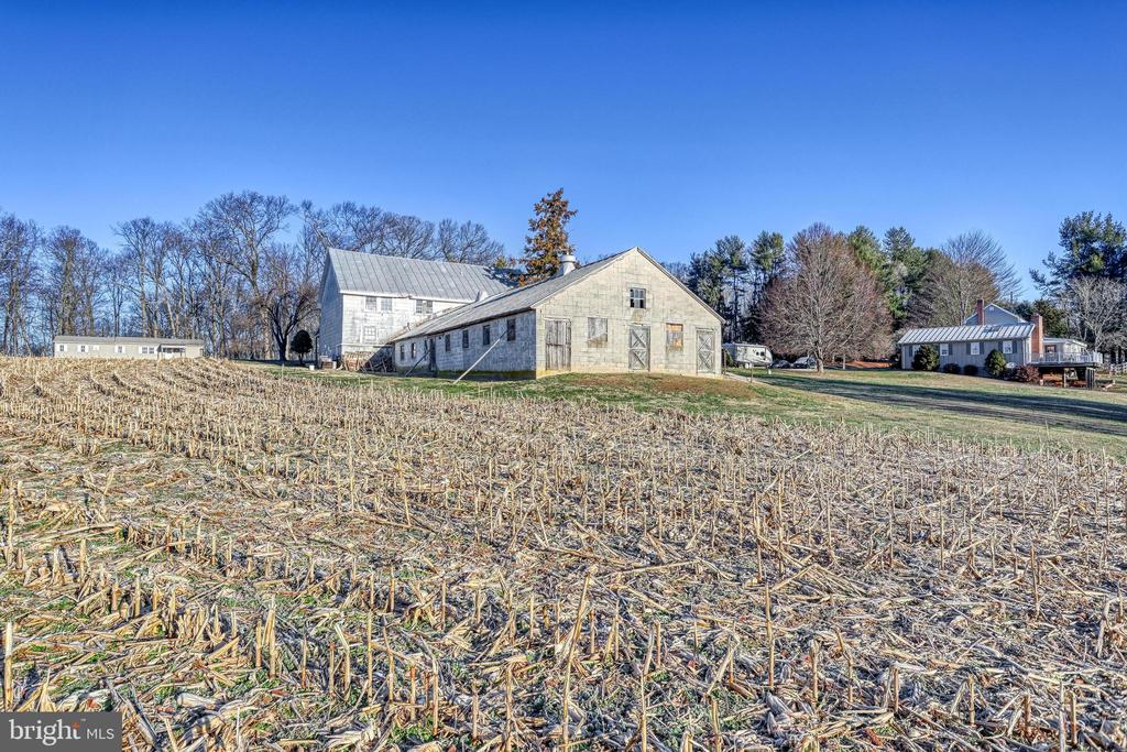 Stone barn and adjoining farm buildings beyond a harvested field.