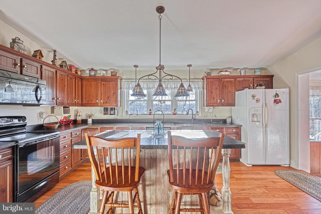 Kitchen with wood cabinetry, a central island, pendant lights, and hardwood flooring.