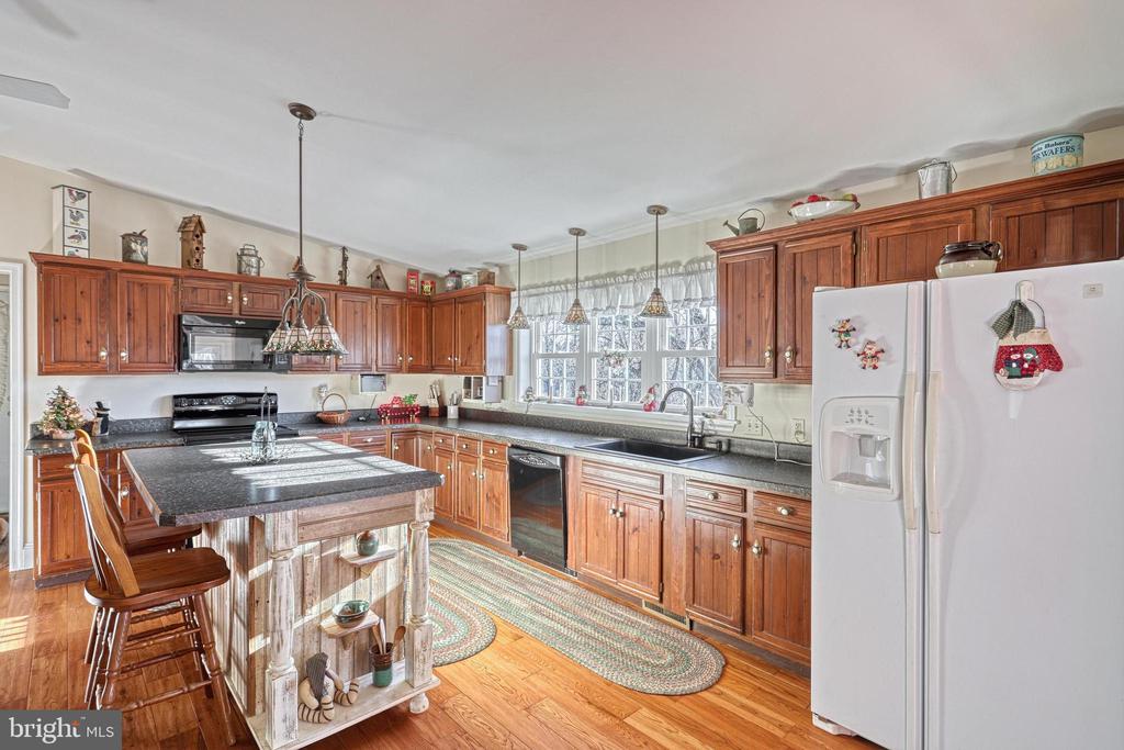 Kitchen with warm wood cabinetry, a stone island, and large windows above the sink.