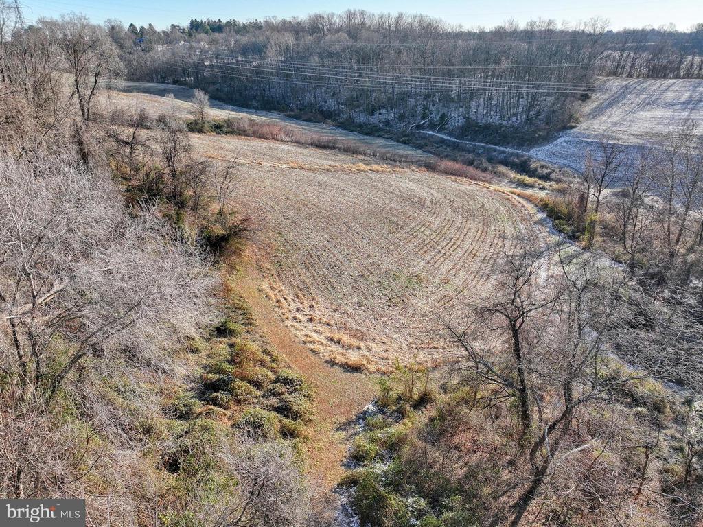 Aerial view of a harvested field bordered by leafless woods and rolling farmland.