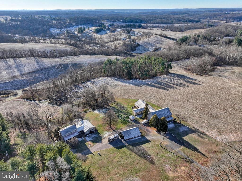 Aerial view of a rural property with farm buildings, open fields, and wooded hills.