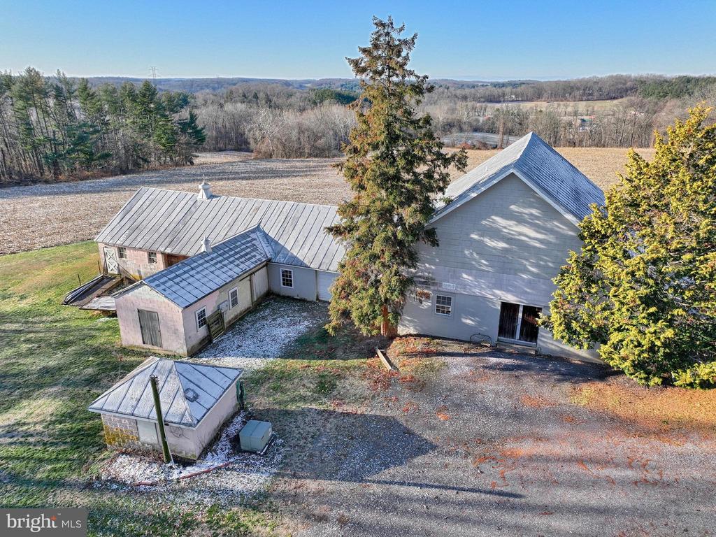 Aerial view of a gray property with metal-roofed outbuildings and open fields.