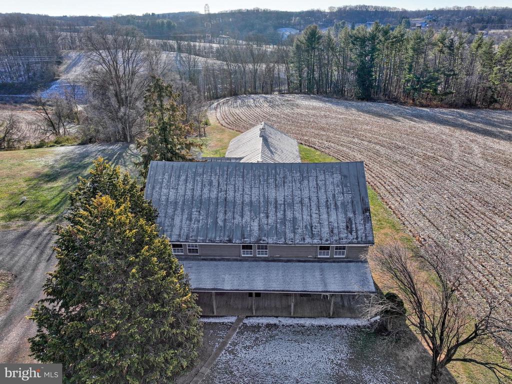 Rural property with a long gray roof beside a plowed field and wooded hills.