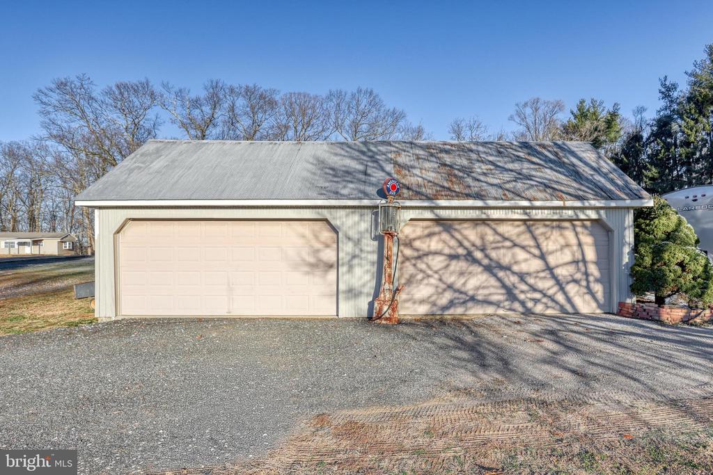 Detached two-bay garage with a metal roof, gravel driveway, and basketball hoop between the doors.