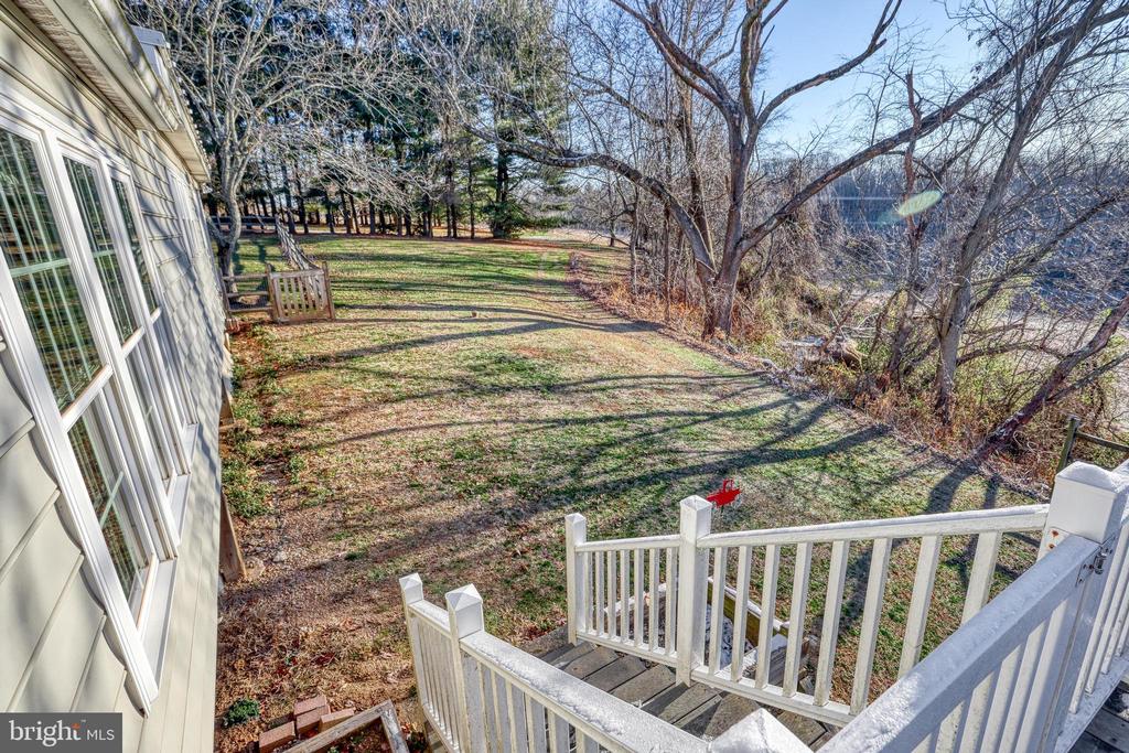 Backyard viewed from a white deck, with a lawn, leafless trees, and woods.
