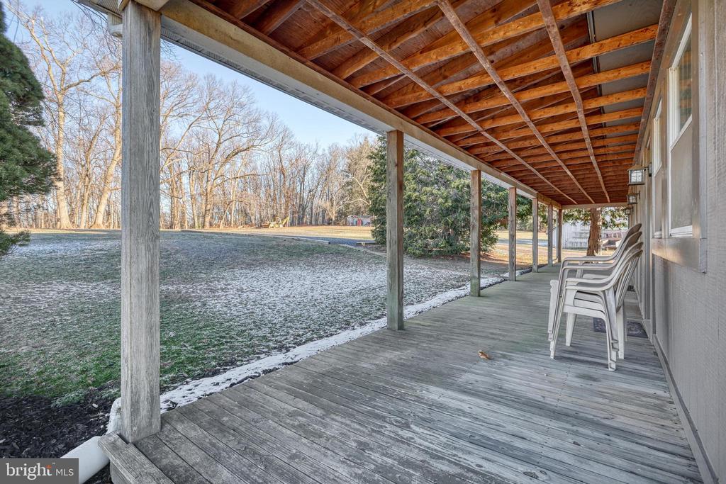 Covered wooden deck with exposed rafters and white chairs overlooking a frosty yard.
