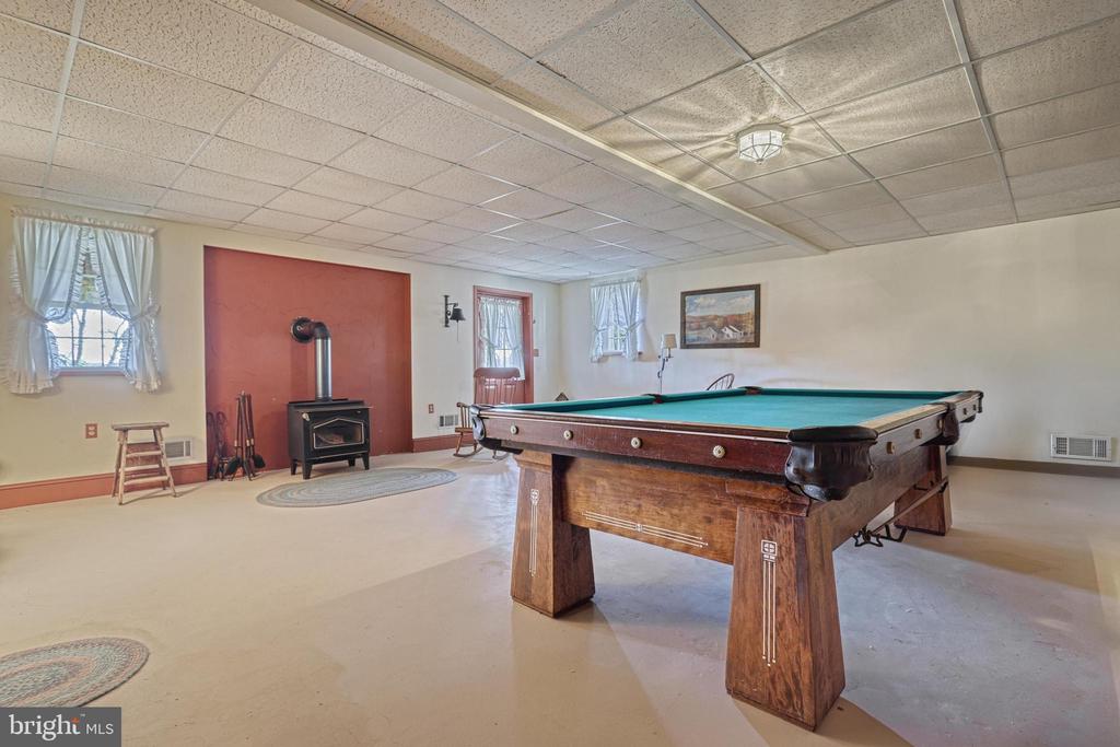 Recreation room with a large wooden pool table and a freestanding stove against a red wall.