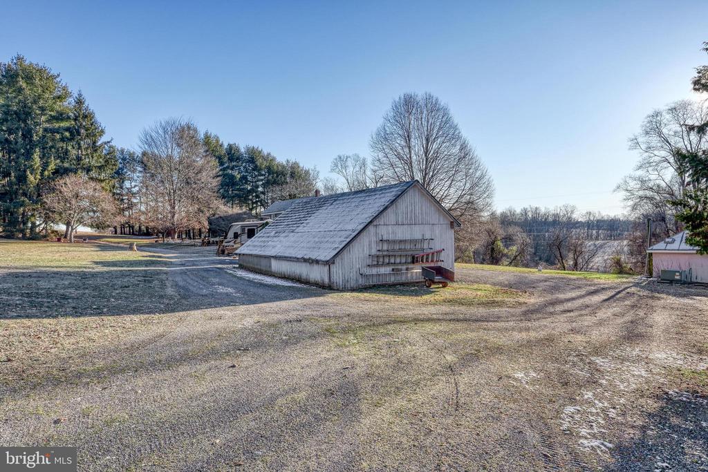 Weathered gray barn beside a gravel yard, with leafless trees and a smaller outbuilding.