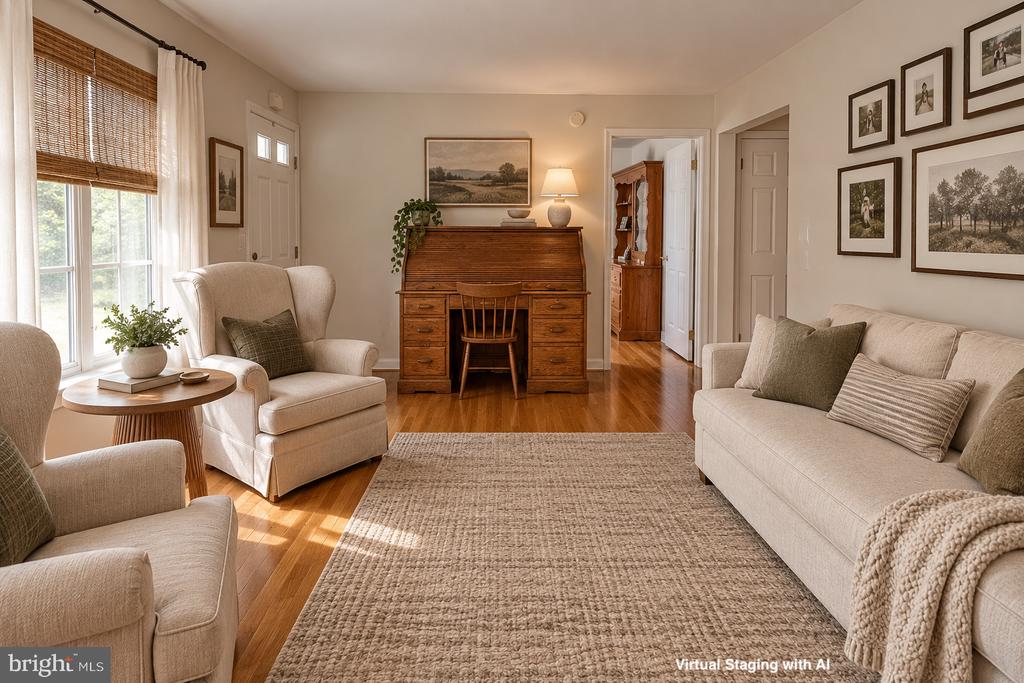 Living room with light sofas, a woven rug, and a wooden writing desk, virtually staged.