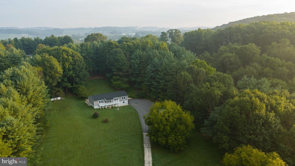 Aerial view of a single-story house and curved driveway in a wooded clearing.