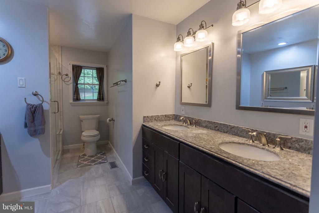 Bathroom with a double vanity, granite countertop, dark cabinets, and glass-enclosed shower.