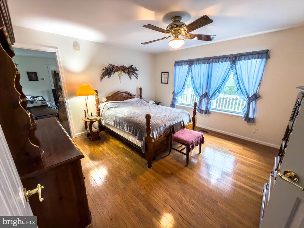 Bedroom with a carved wooden bed, polished hardwood floors, and blue curtains framing a wide window.