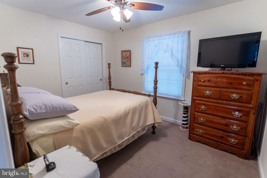 Bedroom with a wooden four-poster bed, curtained window, and television atop a wooden dresser.