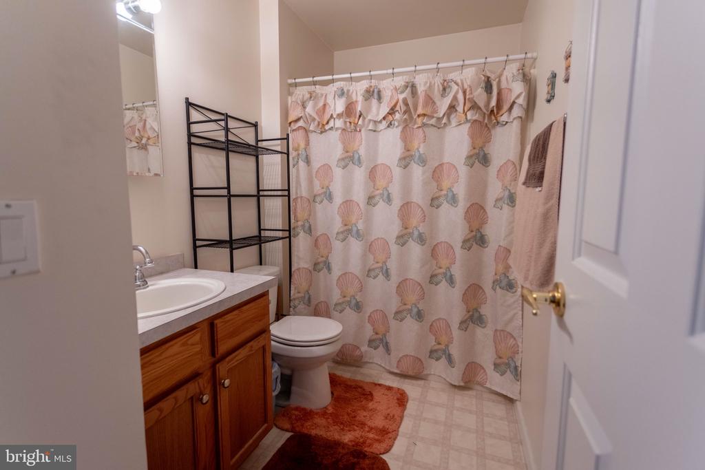 Bathroom with a wood vanity, black metal shelving, and a seashell-patterned shower curtain.