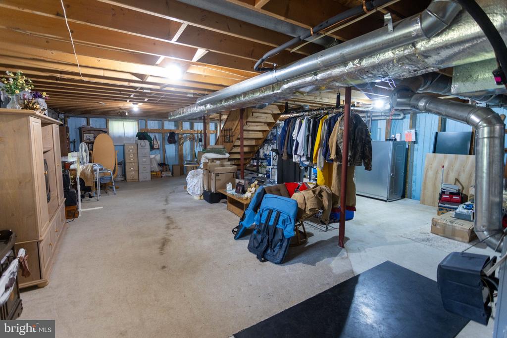 Basement storage area with exposed ceiling joists, large HVAC ducts, boxes, and clothing racks.