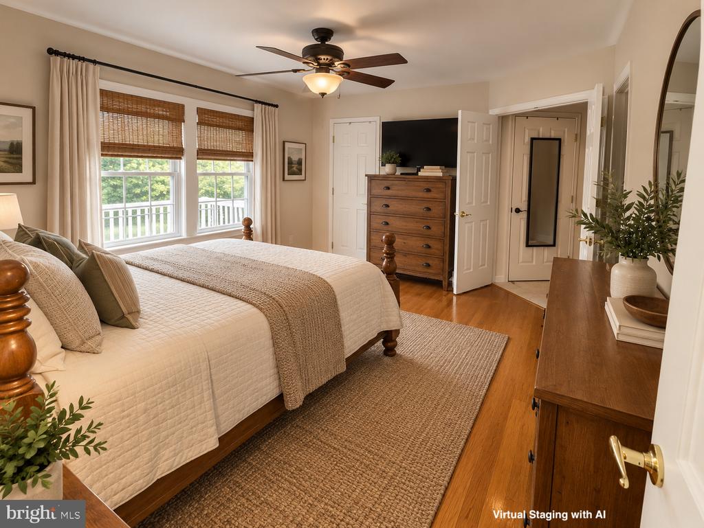 Virtually staged bedroom with cream bedding, woven window shades, a wooden dresser, and hardwood floors.