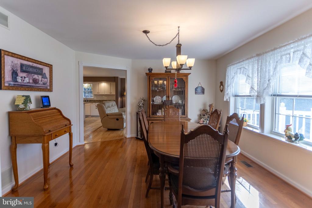 Dining room with a wooden table, glass-front china cabinet, and large lace-curtained windows.