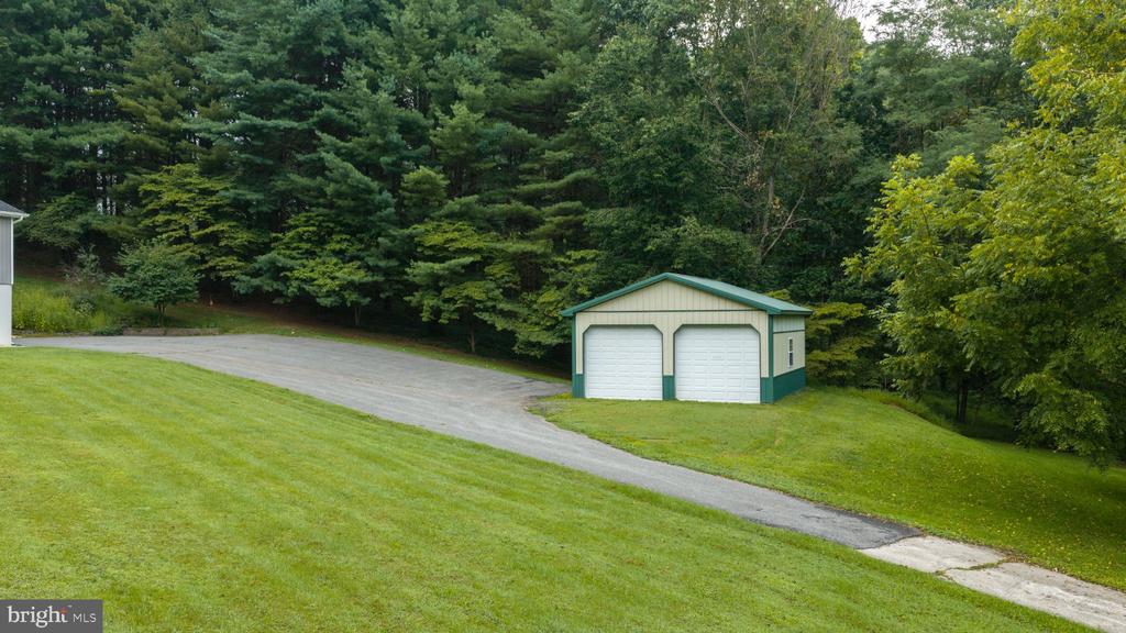 Detached two-bay garage with green trim beside a curved driveway and wooded lawn.